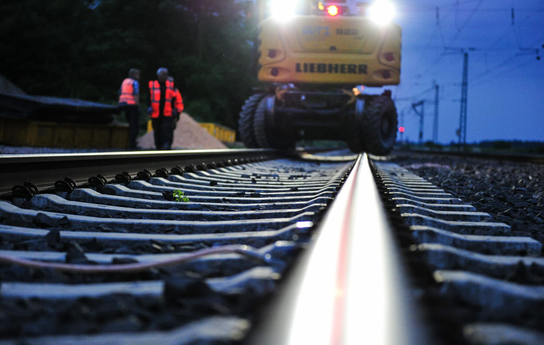 Nächtliche Gleisbaustelle mit Liebherr-Zweiwegebagger und Sicherungsposten
