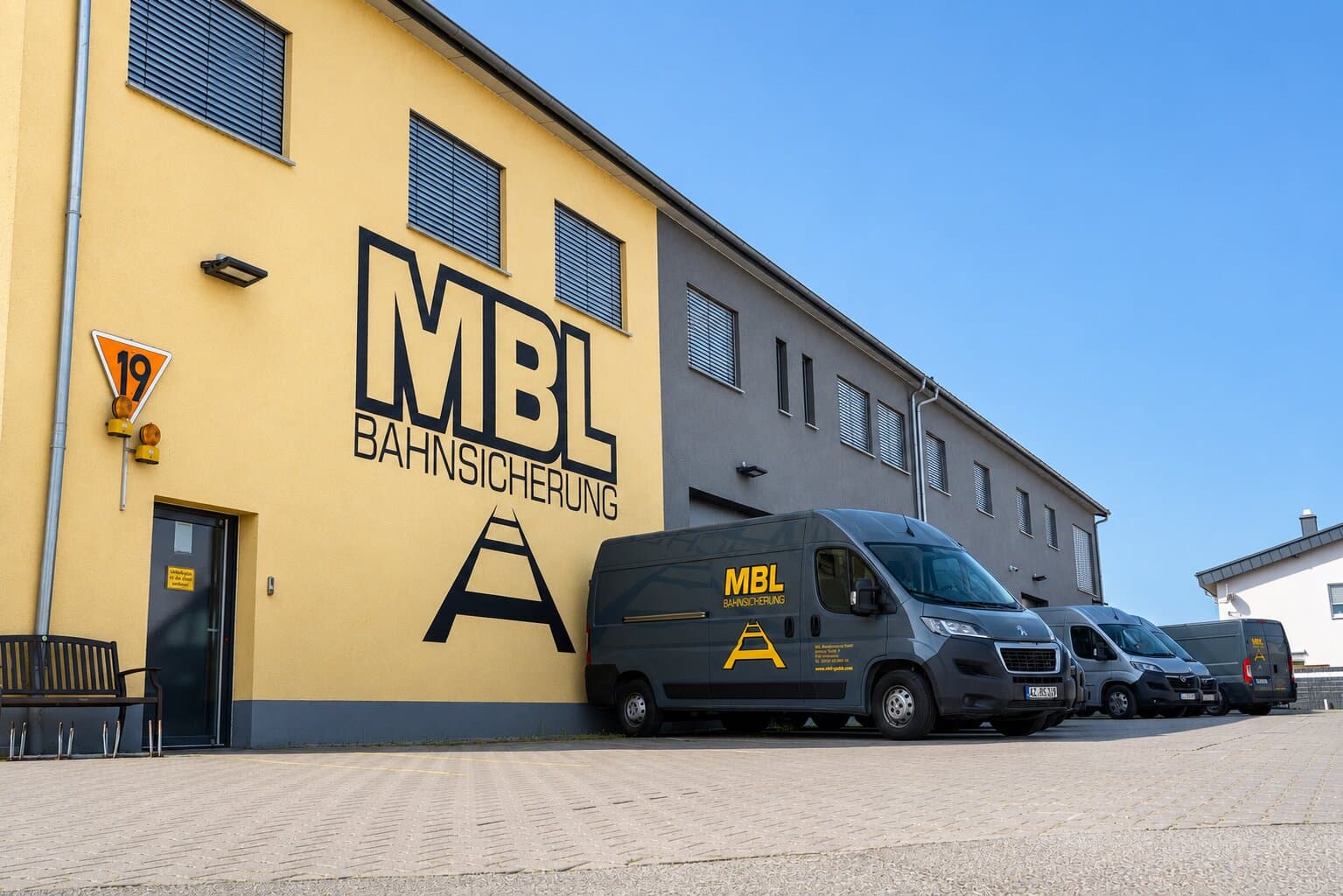 Firmensitz der MBL Bahnsicherung GmbH: gelbe Halle mit Logo und Fuhrpark